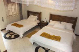 1 Schlafzimmer mit 2 Betten mit weißer Bettwäsche und goldenen Kissen in der Unterkunft Montane Safaris Hotel in Fort Portal