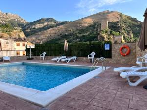 a pool with chairs and a mountain in the background at Alojamientos Peña del Rey in Cazorla