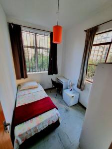 Un dormitorio con una cama y un escritorio y dos ventanas. en Cool Living Hostel - Praça da Liberdade, en Belo Horizonte