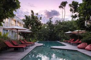 a pool with chairs and umbrellas next to a building at Rimbun Canggu Hotel in Canggu