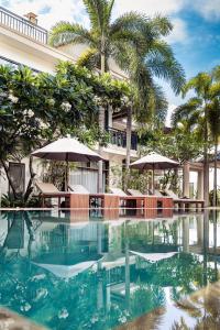 a resort pool with chairs and umbrellas and palm trees at Amatak Boutique Hotel in Siem Reap