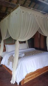 a canopy bed with white sheets and curtains at D'Ume Bendoel Homestay in Jatiluwih