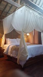 a bedroom with a canopy bed with white sheets at D'Ume Bendoel Homestay in Jatiluwih