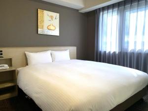 a bedroom with a large white bed and a window at Hotel Route-Inn Isesaki Inter in Isesaki