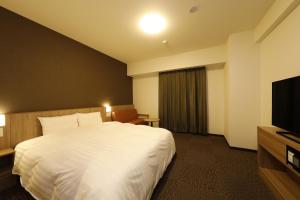 a hotel room with a bed and a flat screen tv at Dormy Inn Maebashi in Maebashi