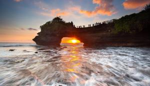 einen Sonnenuntergang über einem Felsbogen im Ozean in der Unterkunft Aster Apartment Bali in Canggu
