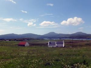 a white barn in a field with mountains in the background at Holiday Home Harlosh by Interhome in Roag