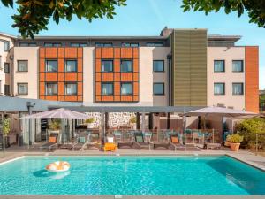 - une piscine avec des chaises et des parasols en face d'un bâtiment dans l'établissement Holiday Inn Toulouse Airport, an IHG Hotel, à Blagnac