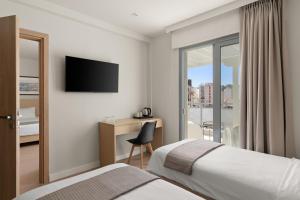 a hotel room with two beds and a desk with a television at Gallery Central Piraeus Port in Piraeus