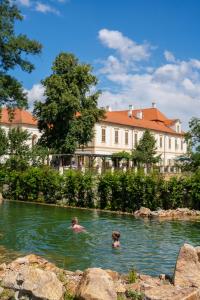due persone che nuotano in un fiume di fronte a un edificio di Maxmilian Lifestyle Resort a Loučeň