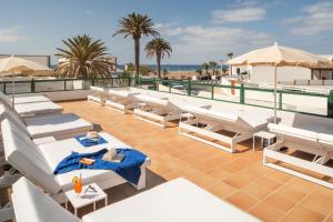 un patio all'ultimo piano con sedie a sdraio bianche e la spiaggia di Hotel Pocillos Playa, solo Adultos a Puerto del Carmen