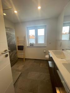 a bathroom with a sink and a toilet and two windows at Haus Gerberstraße - Ferienhäuser Alpenglück in Oberstdorf