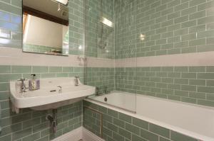 East Harwood Farm Cottage في مينهيد: حمام ذو بلاط أخضر مع حوض استحمام ومغسلة