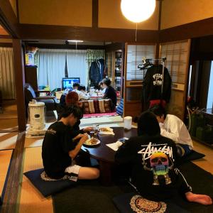 un grupo de personas sentadas alrededor de una mesa comiendo comida en ゲストハウスでたらめ荘, en Yamakami