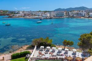 a view of a beach with chairs and boats in the water at Leonardo Royal Hotel Ibiza Santa Eulalia in Es Cana