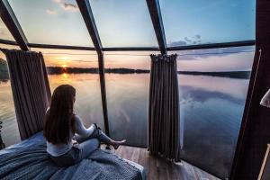a woman sitting on a bed looking out a window at the water at Tackork Gård & Marina in Nauvo