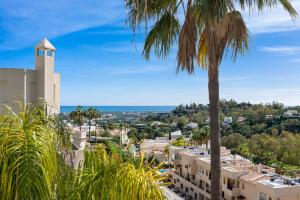 a palm tree and buildings with the ocean in the background at La Quinta Hills - Modern Andalusian-style home with rooftop Terrace in Marbella