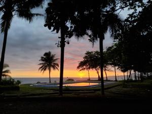 a sunset over the ocean with a pool and palm trees at villa kumala in Tjikakaka