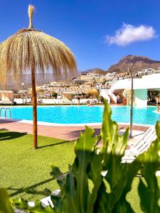 a swimming pool with a straw umbrella and chairs at Sun Island in Adeje