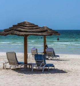 eine Gruppe von Stühlen und einem Sonnenschirm am Strand in der Unterkunft Family rooms with beach view in Ajman 