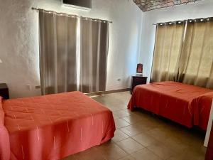 two beds in a room with red sheets and curtains at Casas Rio Mulege in Mulegé