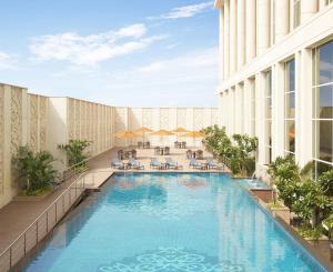 einen Hotelpool mit Tischen und Stühlen in der Unterkunft Taj Santacruz in Mumbai