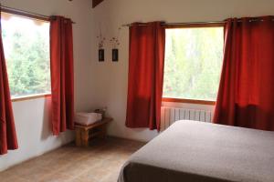 a bedroom with red curtains and a bed and two windows at Alamos del sur Apart hotel in San Carlos de Bariloche
