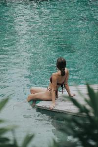 a woman sitting on a dock in the water at Rimbun Canggu Hotel in Canggu