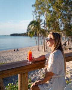 グレート・ケッペルにあるGreat Keppel Island Hideawayの塀に腰掛けて海辺で飲み物を飲む女