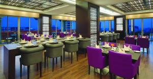 ein Restaurant mit lila Stühlen, Tischen und Fenstern in der Unterkunft Corp Amman Hotel in Amman