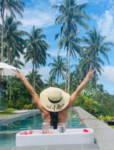 a woman in a hat sitting in front of a swimming pool at Bintana sa Paraiso Binunsaran in Mambajao