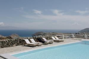 a pool with chairs and the ocean in the background at Mykonos Supreme Comfort Suites & Villas in Kalafatis