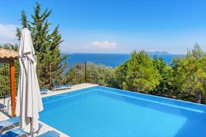 a blue swimming pool with an umbrella and the ocean at Villa Columba - Luxury Private Villa in Modern Residence in Sivota