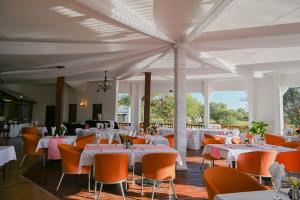 a dining room with white tables and orange chairs at Pioneer lodge in Lephalale