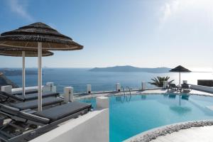 a swimming pool with chairs and an umbrella and the ocean at Santorini Princess Spa Hotel in Imerovigli