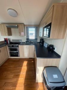 a small kitchen with wooden cabinets and a black counter top at Lyons robin hood caravan 43SW in Rhyl +2 photos