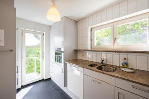 La cuisine est équipée de placards blancs, d'un évier et de fenêtres. dans l'établissement Ferienhaus Rütiboda bis 17 Personen, à Davos