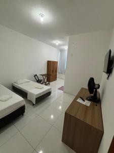 a room with two beds and a table and a tv at Shalom Flat Hotel in Pará de Minas