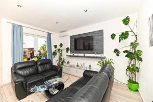 a living room with a black leather couch and a tv at Apartmani Dolores in Kaštela