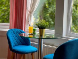 a glass table with two blue chairs and a drink at Timbertop Suites - Adults Only in Weston-super-Mare