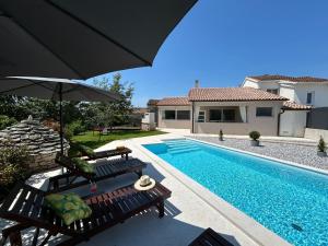 a pool with two benches and an umbrella next to a house at Holiday house Diva with a pool in Svetvinčenat