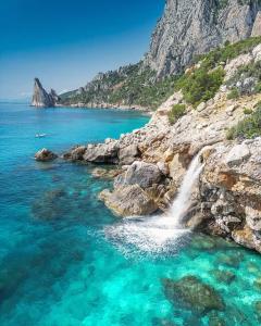 a waterfall on a rocky shore with blue water at Lungomare Bed rooms in Santa Maria Navarrese