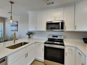 a kitchen with white cabinets and a sink and a microwave at Serenity Now in Topsail Beach