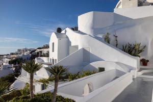 a white house with palm trees in front of it at IKIES Santorini in Oia