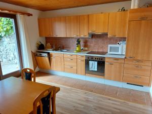 cocina con armarios de madera, mesa y microondas en Ferienwohnung Tschengla mit eigener Sonnenterrasse - Wiese - Wlan - Netflix, en Bürserberg