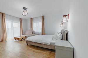 a white bedroom with a bed and a chair at Villa Russo in Râşnov