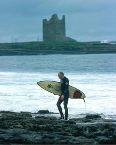 Ein Mann steht am Strand und hält ein Surfbrett. in der Unterkunft Seafront House in Sligo + 14 Fotos
