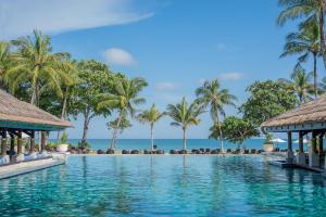 a swimming pool with palm trees and the ocean at InterContinental Bali Resort by IHG in Jimbaran