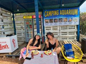 deux femmes assises à une table devant un magasin dans l'établissement Camping Aquarium, à Himarë