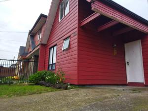 a red house with a white door and a fence at Casa Valle Volcanes 3 Dormitorios in Puerto Montt